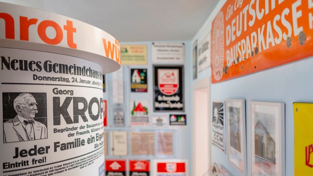 Litfasssäule mit einer Veranstaltzung von Georg Kropp, im Hintergrund verschiedene Werbeplakate und Blechschilder